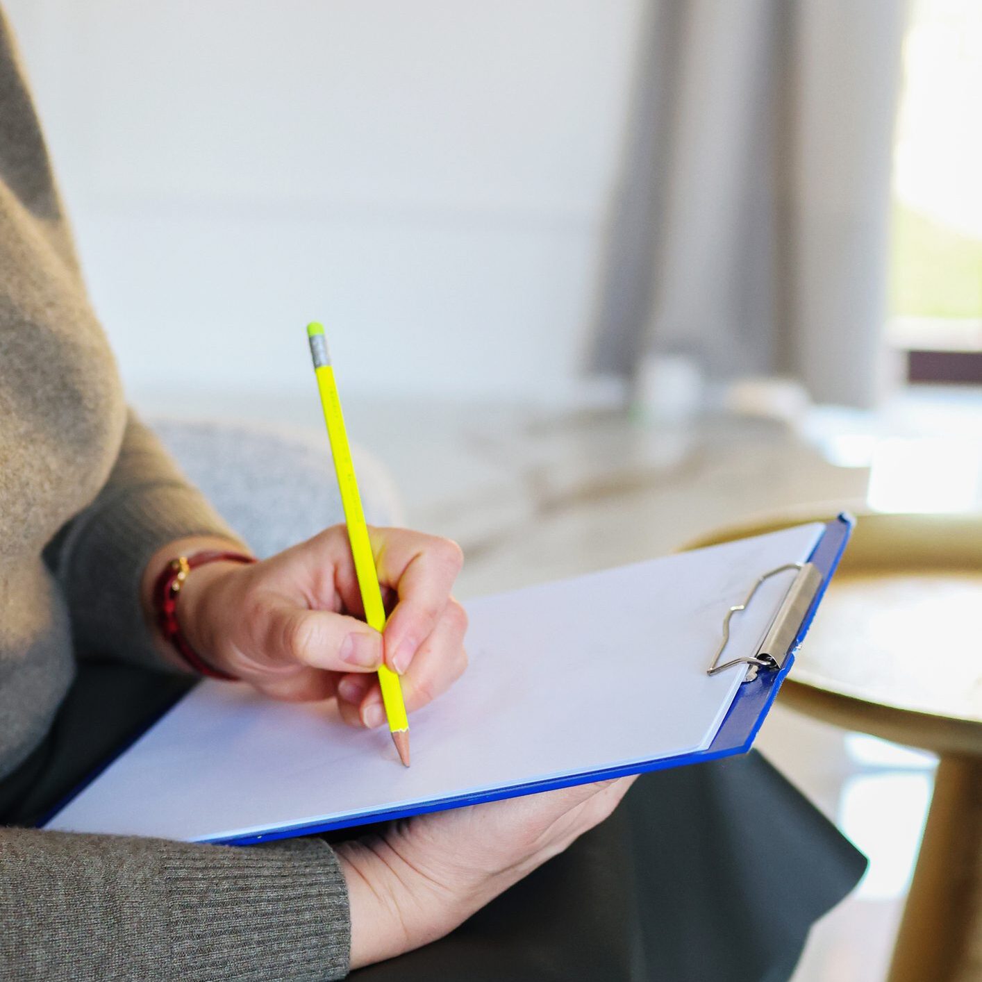Person writing on clipboard with pencil.
